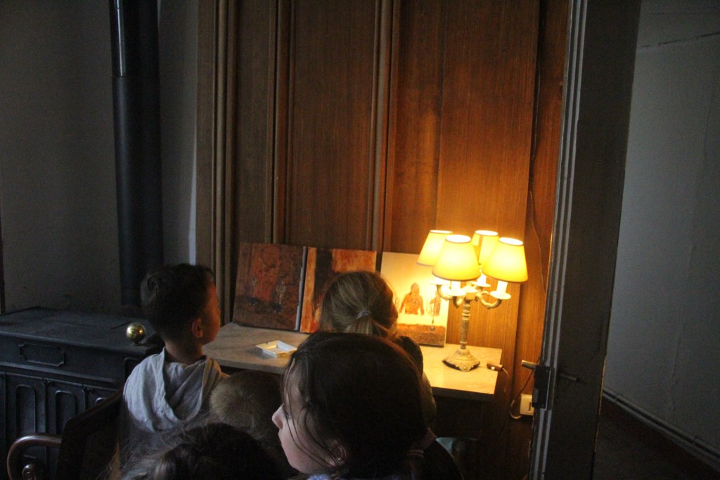 Children observing artwork in a castle setting, with a lamp illuminating the scene. Château de Bouillancourt-en-Séry