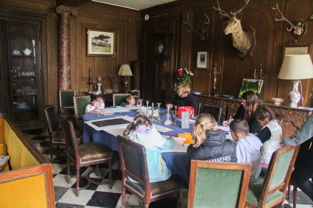 Children participating in an art activity at a dining table in a historical room, with a focus on drawing and creativity.